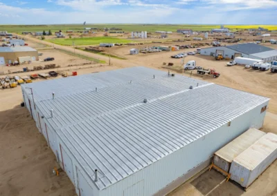 Aerial view of a large industrial building with a metal roof, surrounded by construction equipment and vehicles in a rural area.