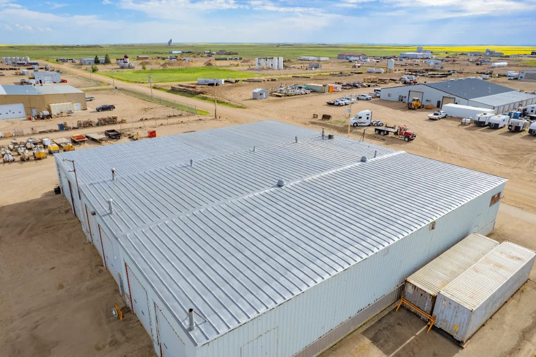 TKCRETOUCHED (1) Aerial view of a large industrial building with a metal roof, surrounded by construction equipment and vehicles in a rural area.